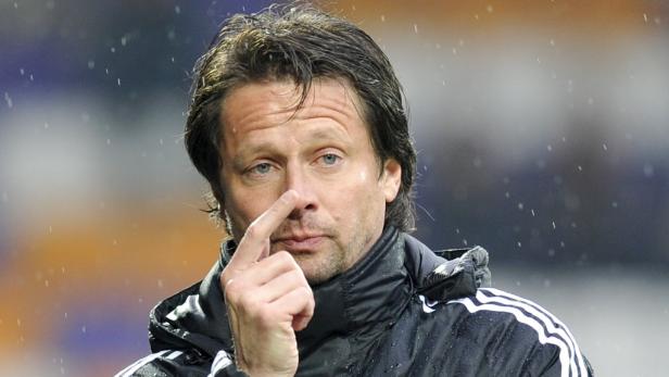 Ein Mann mit dunklen Haaren und einer schwarzen Jacke berührt seine Nase.