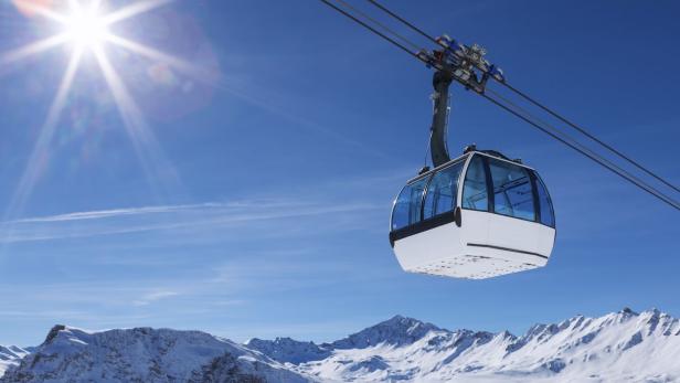 Eine Gondel schwebt vor schneebedeckten Bergen unter einem strahlend blauen Himmel.