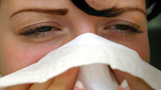 Eine Frau putzt sich mit einem Papiertaschentuch die Nase.