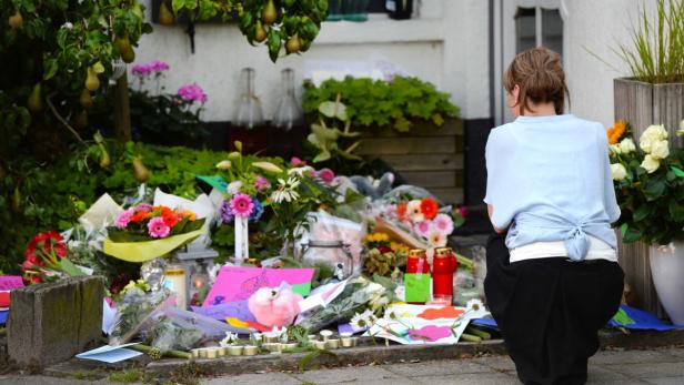 Eine Frau kniet vor einer Gedenkstätte mit Blumen, Kerzen und Zeichnungen.
