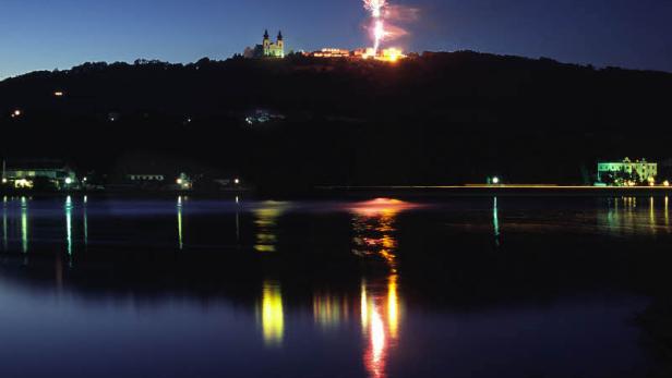 Feuerwerk über einem Hügel mit einer Kirche, gespiegelt im Wasser.
