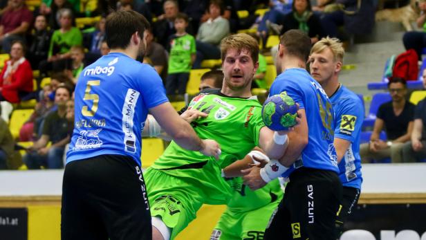 Ein Handballtorwart in grüner Sportkleidung wird von mehreren Spielern umringt.