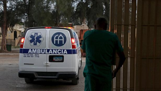 Ein Sanitäter geht in ein Gebäude, während ein Krankenwagen im Hintergrund parkt.