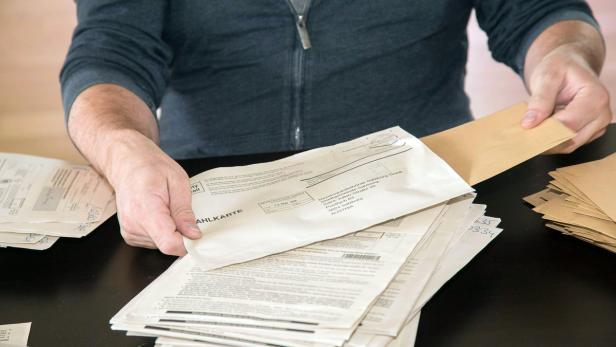 Eine Person steckt eine Wahlkarte in einen Umschlag.