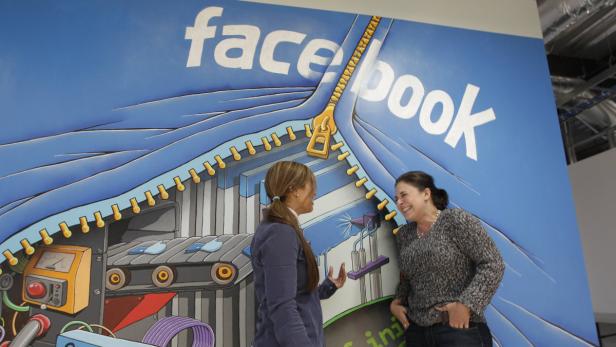 Zwei Frauen unterhalten sich vor einer Wandmalerei mit dem Facebook-Logo und einer Fabrikszene.