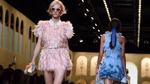 Eine Frau in einem rosa Federkleid auf dem Laufsteg einer Modenschau.