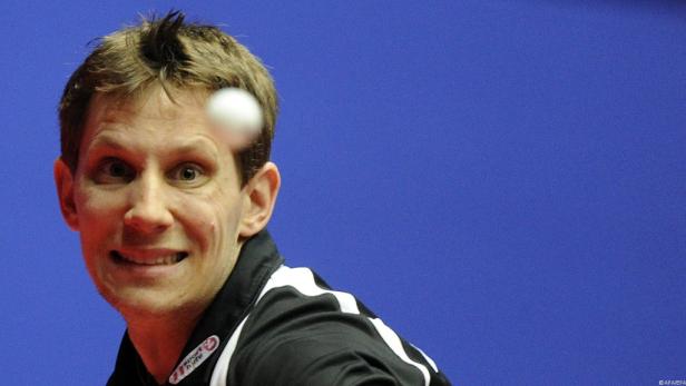 Ein Tischtennisspieler beim Aufschlag vor blauem Hintergrund.