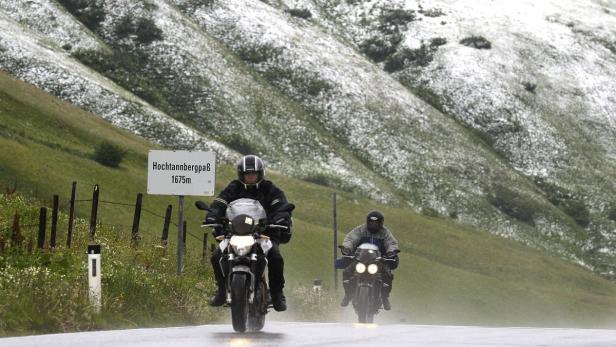 Zwei Motorradfahrer fahren auf einer nassen Straße am Hochtannbergpass.