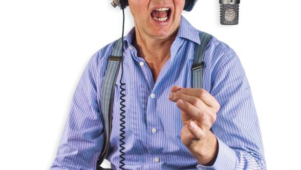 Ein Mann mit Kopfhörern gestikuliert vor einem Mikrofon.