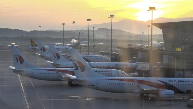 Mehrere Flugzeuge der Malaysia Airlines stehen bei Sonnenaufgang auf einem Flughafen.