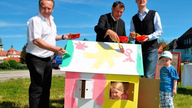 Drei Erwachsene und zwei Kinder bemalen ein kleines Spielhaus im Freien.