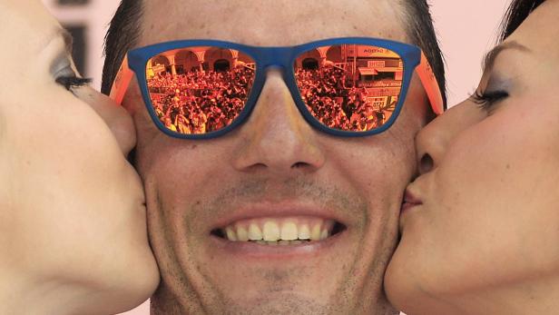 Ein Mann wird von zwei Frauen auf die Wange geküsst, im Spiegelbild seiner Sonnenbrille ist eine Menschenmenge zu sehen.