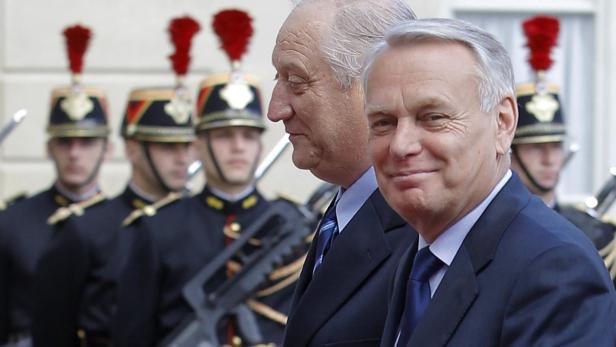 Zwei Männer in Anzügen stehen vor einer Reihe von Soldaten in Paradeuniformen.