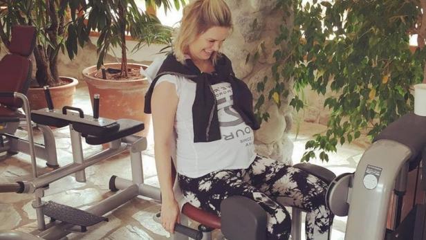 Eine Frau trainiert an einer Beinpresse in einem Fitnessstudio mit Pflanzen und Steindekor.