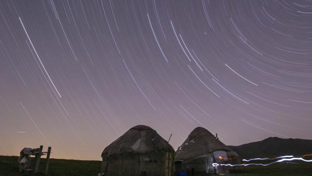 Zwei Jurten stehen unter einem Sternenhimmel mit langen Belichtungsspuren.