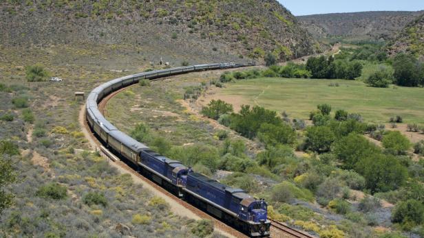 Ein blauer Zug fährt durch eine grüne Landschaft.