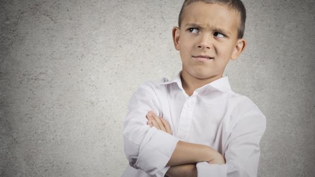 Ein Junge mit verschränkten Armen und skeptischem Blick schaut zur Seite.