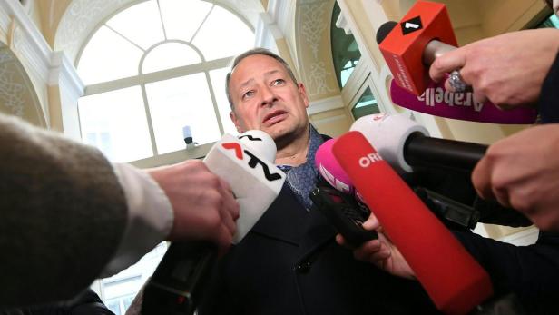 Ein Mann wird von Reportern mit Mikrofonen umringt.