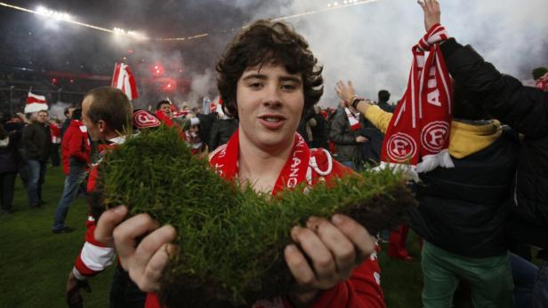 Ein junger Mann hält ein Stück Rasen in einem Fußballstadion hoch.