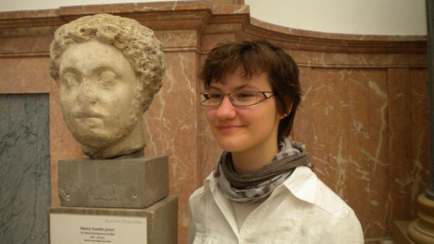 Eine junge Frau steht neben einer Büste von Marco Aurelio in einem Museum.