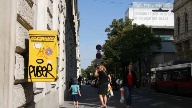 Ein gelber Briefkasten mit Graffiti an einer Straße in Wien.