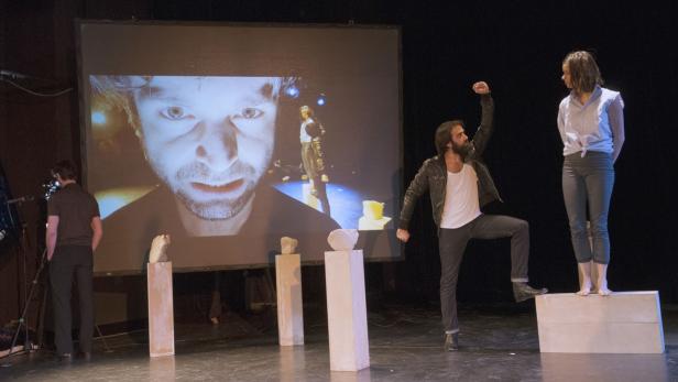 Auf einer Bühne interagieren zwei Schauspieler vor einer Videoprojektion.
