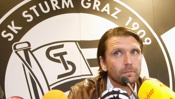 Ein Mann steht vor dem Logo des SK Sturm Graz und spricht in mehrere Mikrofone.
