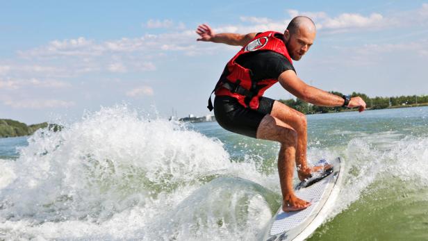 Ein Mann mit roter Schwimmweste wakesurft auf einem See.