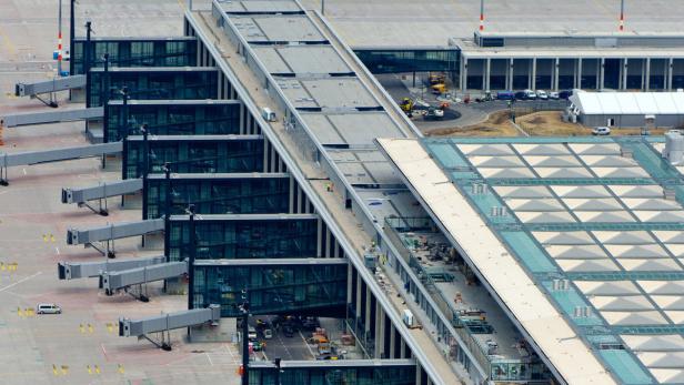 Luftaufnahme eines Flughafens mit Flugsteigen und einem Gebäude mit dreieckigen Oberlichtern.