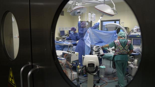 Ein Blick durch eine Tür in einen Operationssaal mit medizinischem Personal bei der Arbeit.