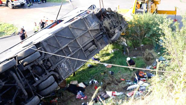 Ein umgestürzter Bus liegt auf der Seite, während Rettungskräfte am Unfallort arbeiten.