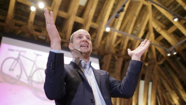 Ein Mann mit Mikrofon gestikuliert vor einer Präsentation mit einem Fahrrad.