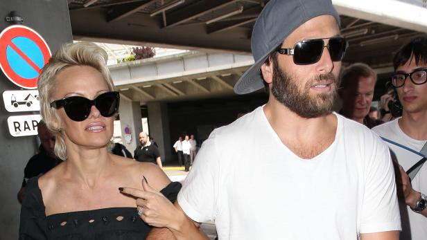 Pamela Anderson und ein Mann mit Bart und Kappe stehen zusammen im Freien.