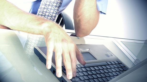 Ein Mann im Hemd und mit Krawatte tippt auf einem Laptop.