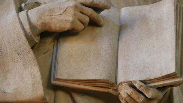 Die Hände einer Statue halten ein offenes Buch.