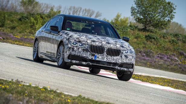 Ein BMW mit Tarnmuster fährt auf einer kurvenreichen Straße.