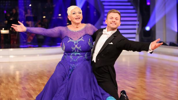 Ein Tanzpaar in festlicher Kleidung posiert auf einer Bühne.