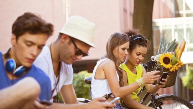Eine Gruppe junger Leute sitzt im Freien und benutzt ihre Smartphones.