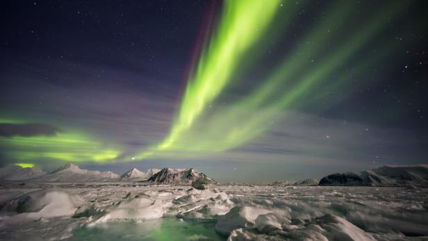 Grüne Nordlichter erhellen den Himmel über einer verschneiten Landschaft.