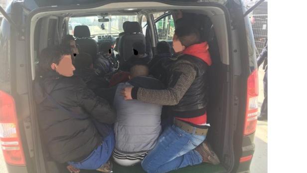 Mehrere Personen sind eng in den Laderaum eines schwarzen Vans gepfercht.