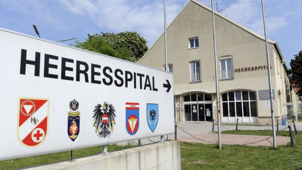 Ein Schild mit der Aufschrift „Heeresspital“ und verschiedenen Wappen vor einem Krankenhausgebäude.
