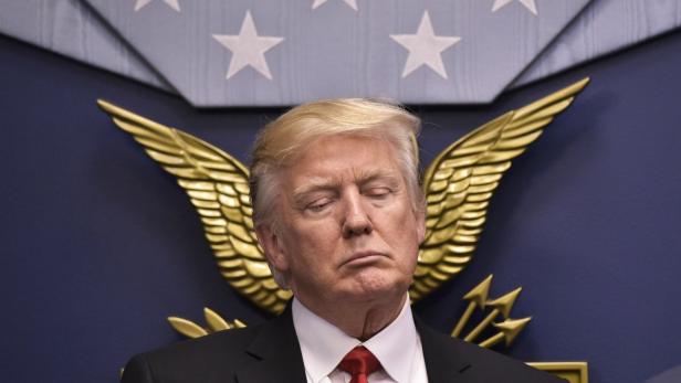 Donald Trump mit geschlossenen Augen vor einem blauen Hintergrund mit goldenen Flügeln.