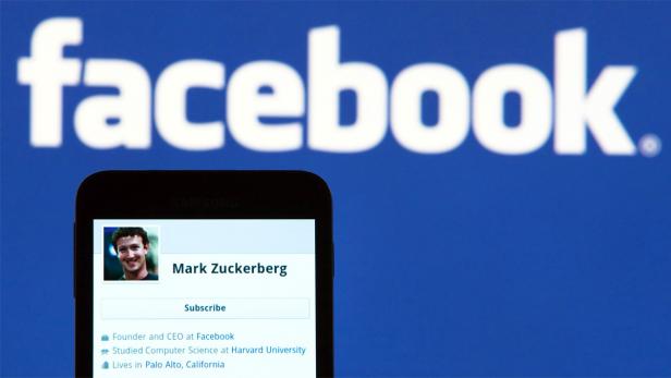 Ein Smartphone zeigt das Facebook-Profil von Mark Zuckerberg vor dem Facebook-Logo.