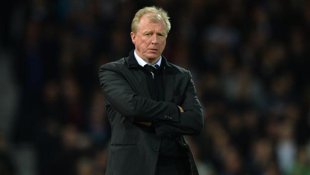 Ein Mann mit verschränkten Armen in einem dunklen Anzug.