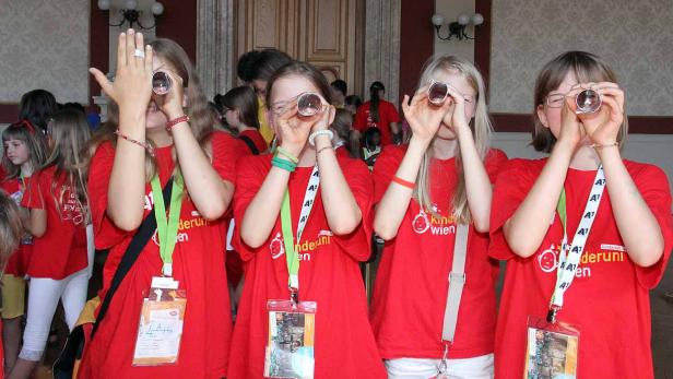 Eine Gruppe von Mädchen mit roten T-Shirts blickt durch kleine Röhren.