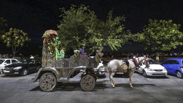 Eine geschmückte Pferdekutsche steht nachts auf einer Straße, umgeben von geparkten Autos.