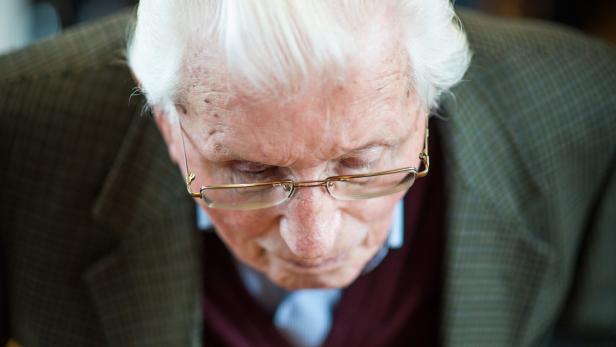 Ein älterer Mann mit Brille blickt nach unten.