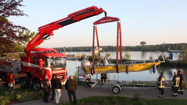 Ein Feuerwehrkran hebt ein gelbes Rettungsboot über einen Fluss.