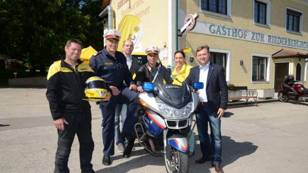 Eine Gruppe von Personen posiert vor einem Gasthof mit einem Polizeimotorrad.