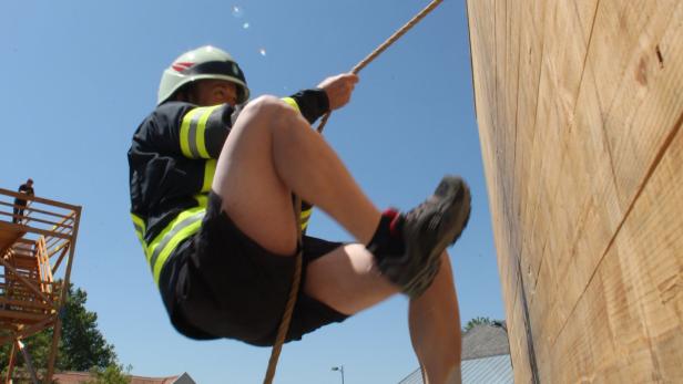 Ein Feuerwehrmann seilt sich an einer Holzwand ab.